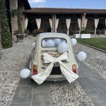 Fiat 500 decorata con palloncini bianchi e fiocco per il matrimonio, nel cortile della location
