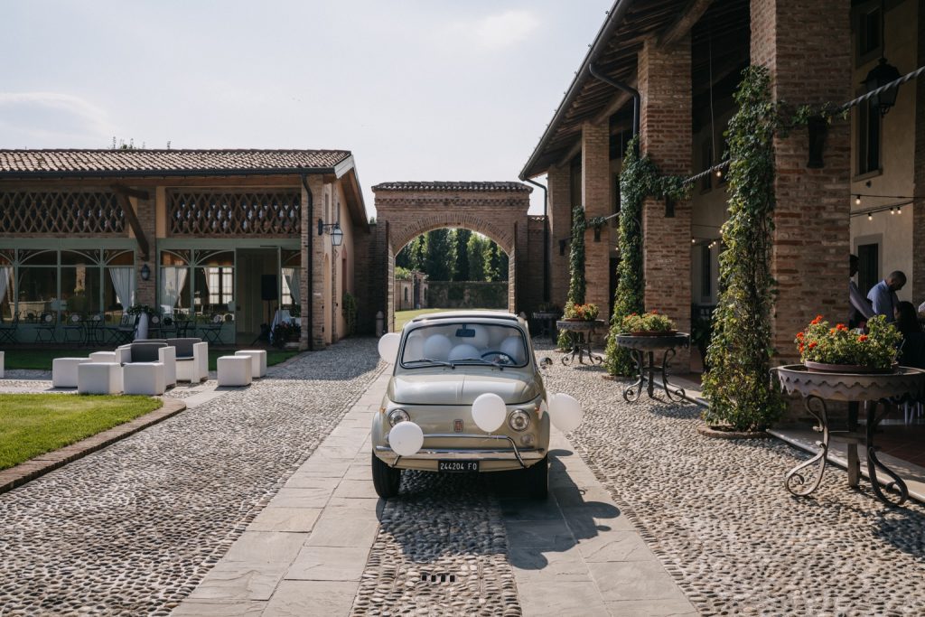 Fiat 500L d'epoca color avorio in ingresso a una location di matrimonio, sotto un arco in mattoni